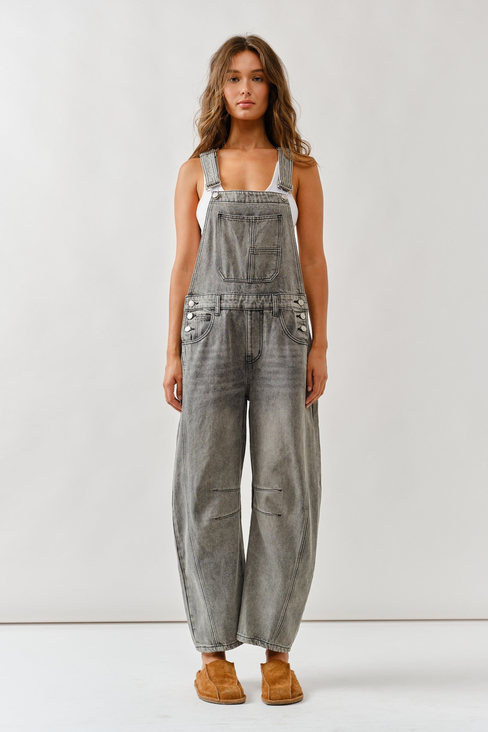 Person wearing gray denim overalls on a white background