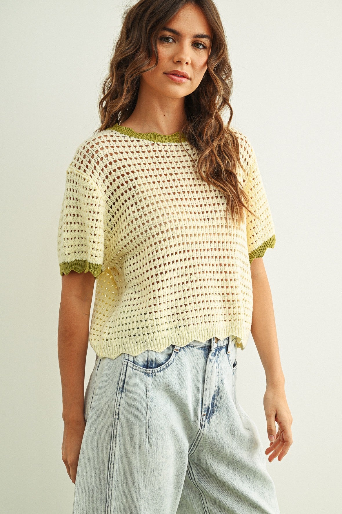 Woman wearing a yellow crochet top and light blue jeans on a plain background