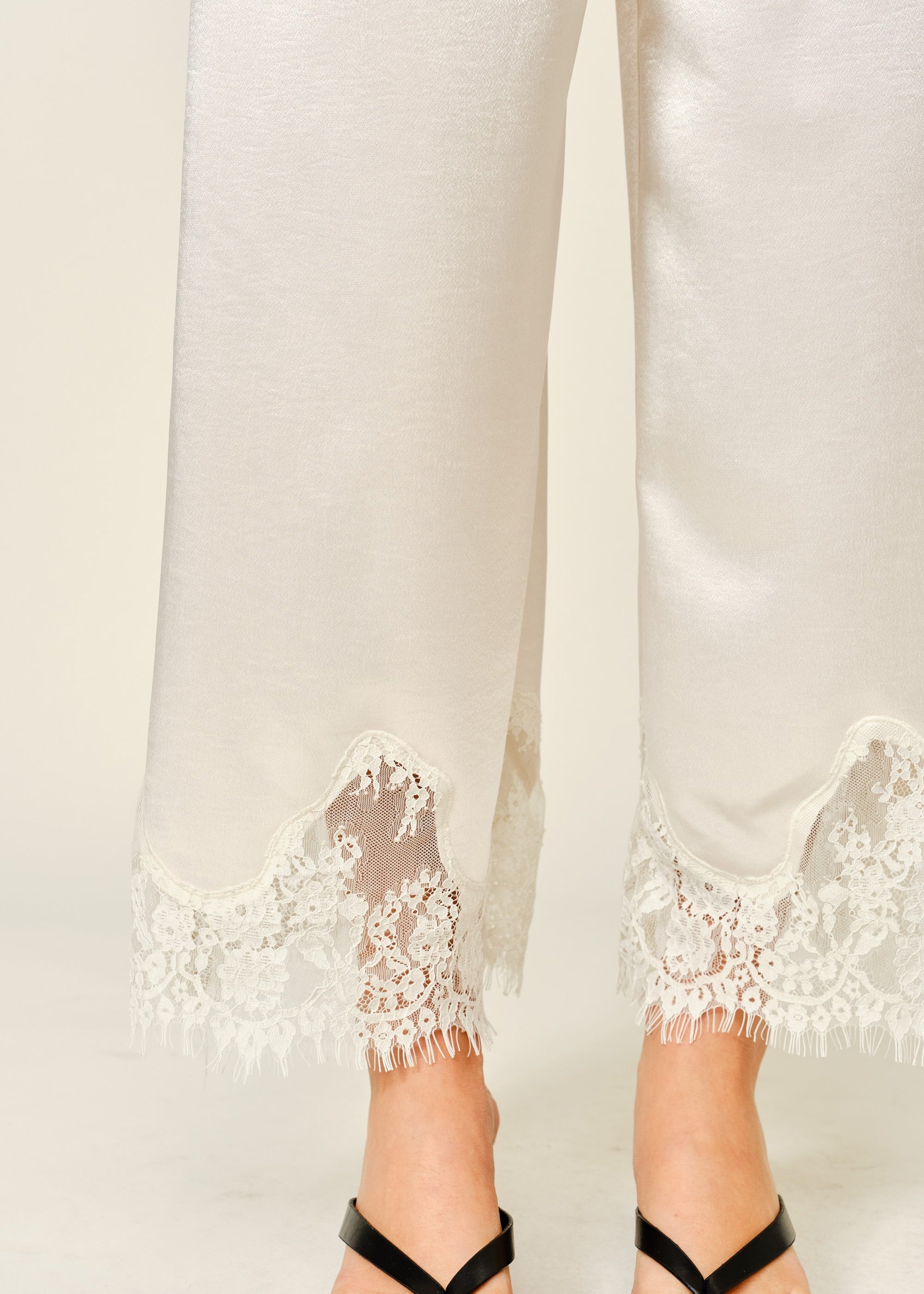 Close-up of champagne satin pants with delicate lace trim hem detail