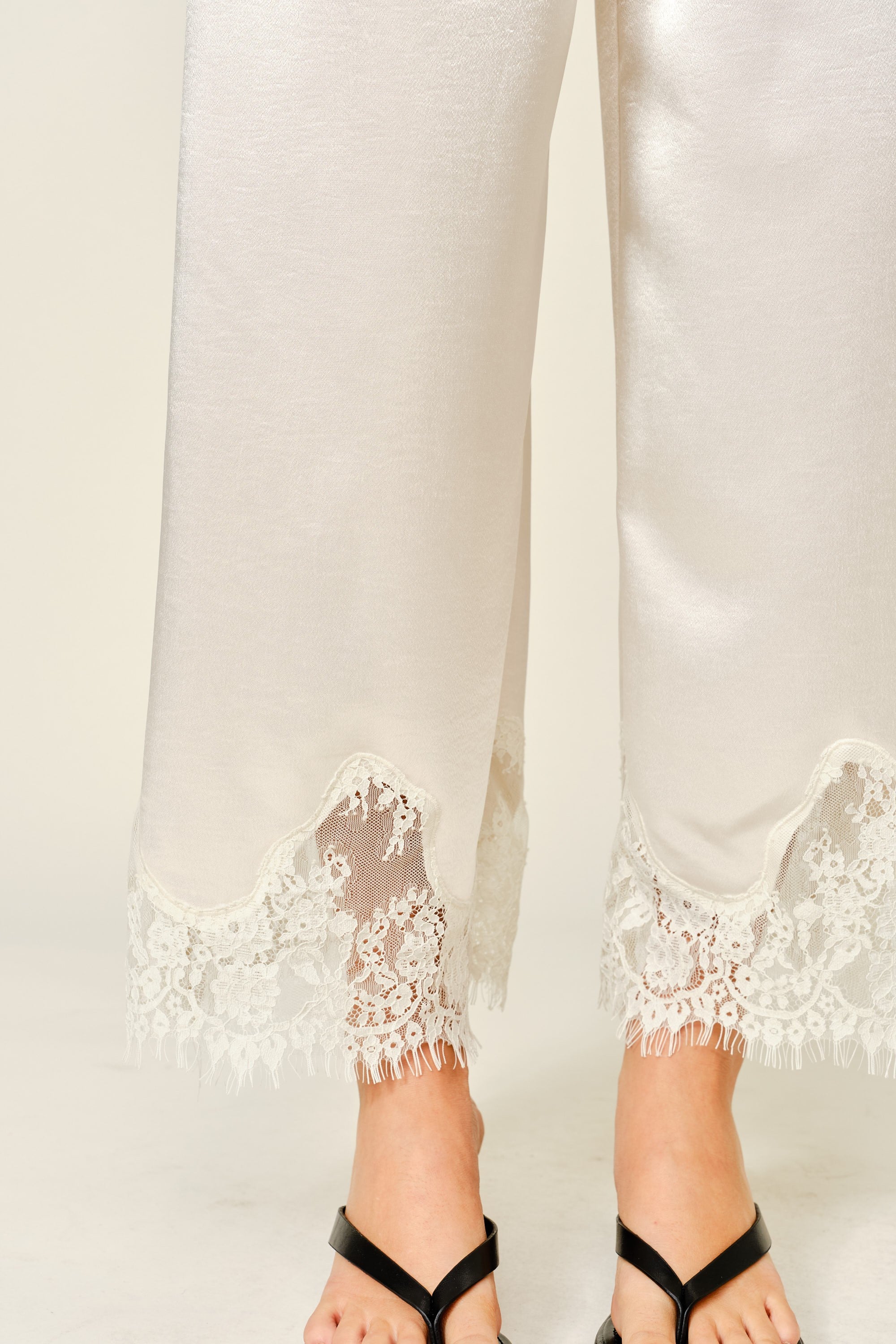 Close-up of champagne satin pants with delicate lace trim hem detail