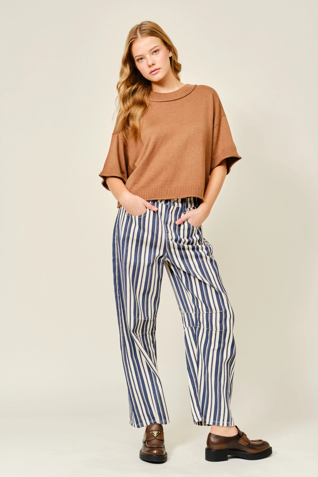 Woman wearing a brown top and striped pants on a plain background