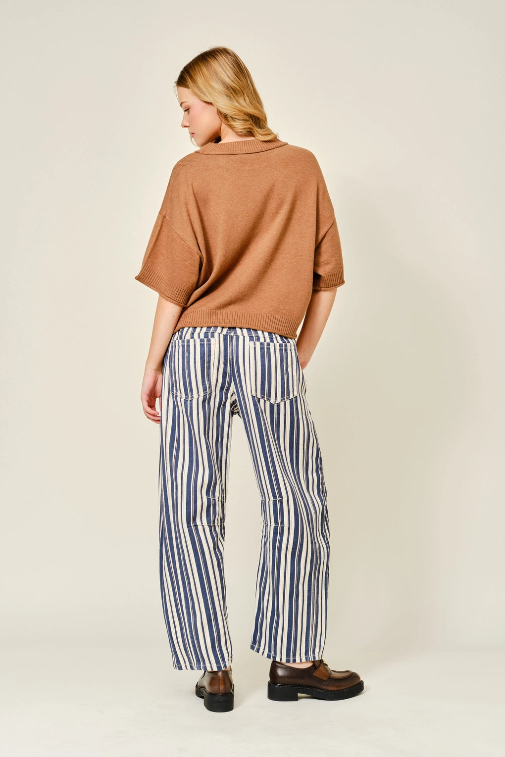 Woman wearing a brown sweater and striped pants on a beige background