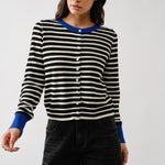 Woman wearing a black and white striped sweater with blue cuffs and collar against a white background