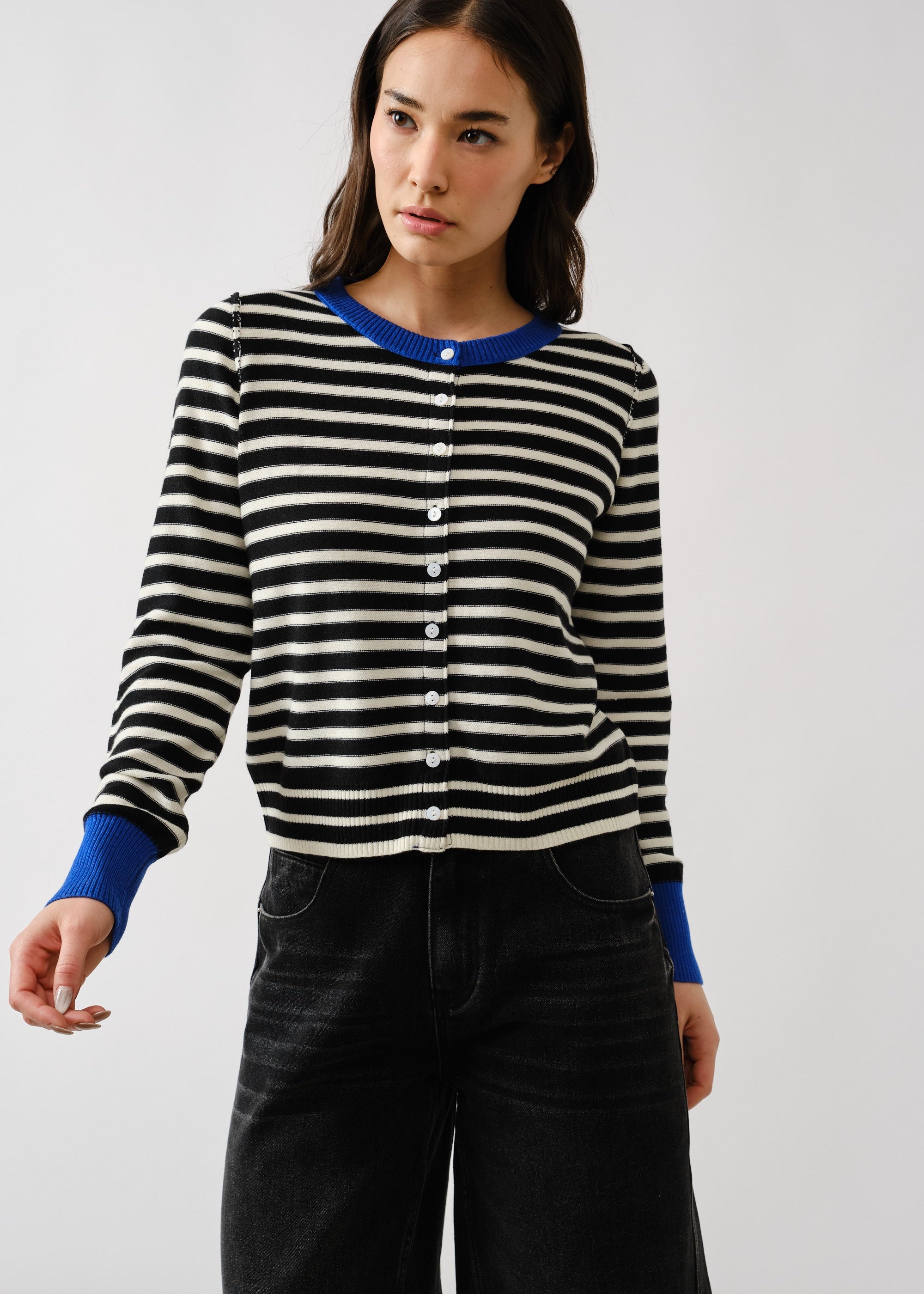 Woman wearing a black and white striped sweater with blue cuffs and collar against a white background