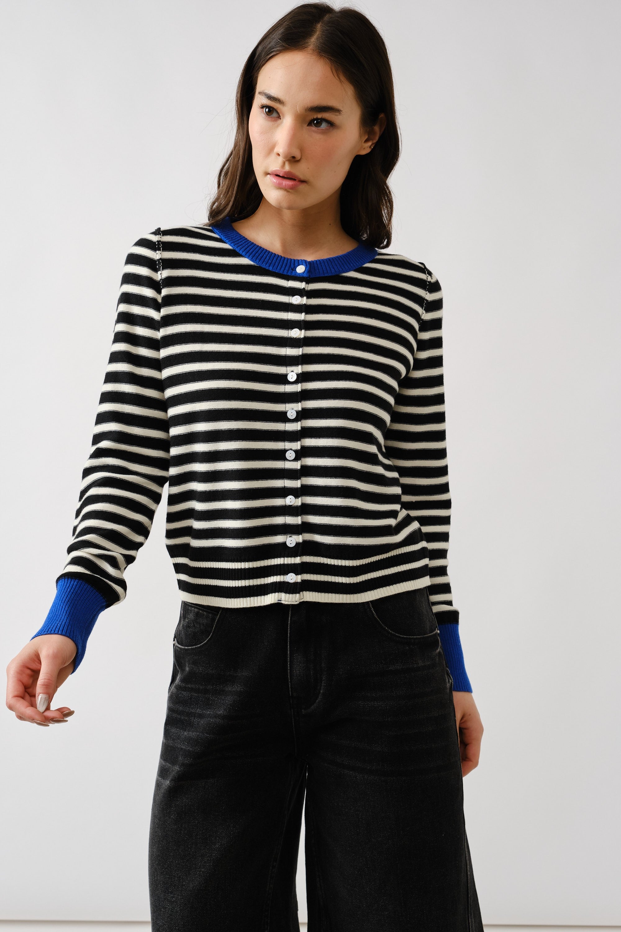 Woman wearing a black and white striped sweater with blue cuffs and collar against a white background