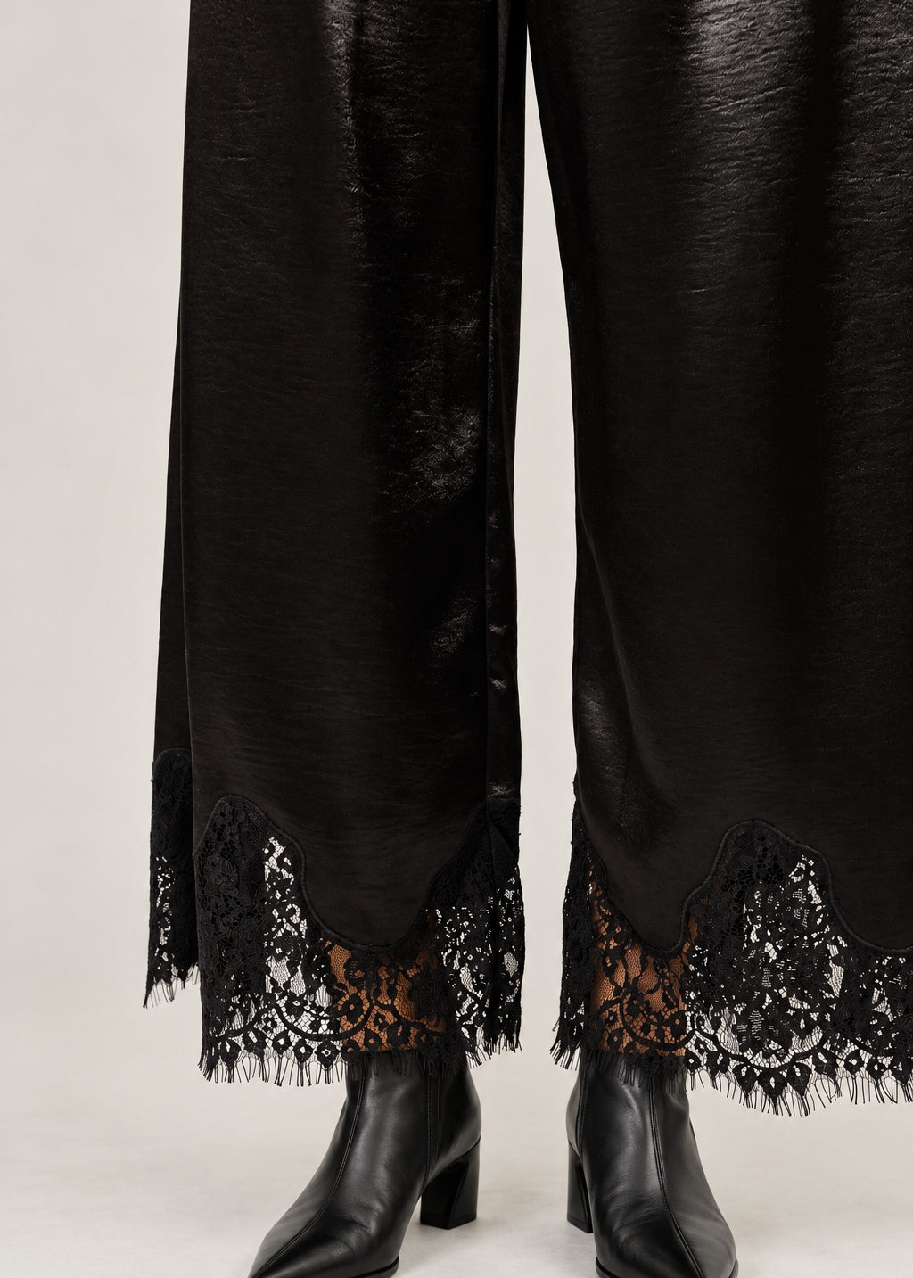 Lower-leg detail of Heirloom black satin pants showing the wide cut and delicate lace hems.