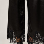 Lower-leg detail of Heirloom black satin pants showing the wide cut and delicate lace hems.