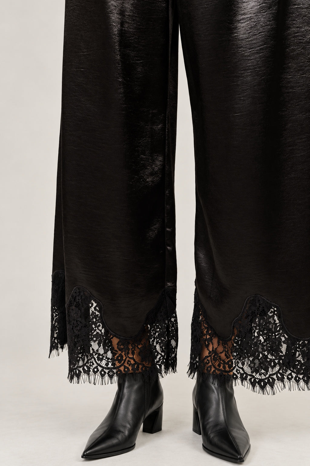 Lower-leg detail of Heirloom black satin pants showing the wide cut and delicate lace hems.