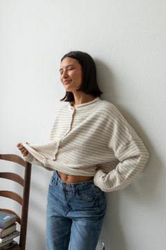 Woman wearing Hailey Button Down Cardigan – Cream Mini Striped  and blue jeans against a white wall.