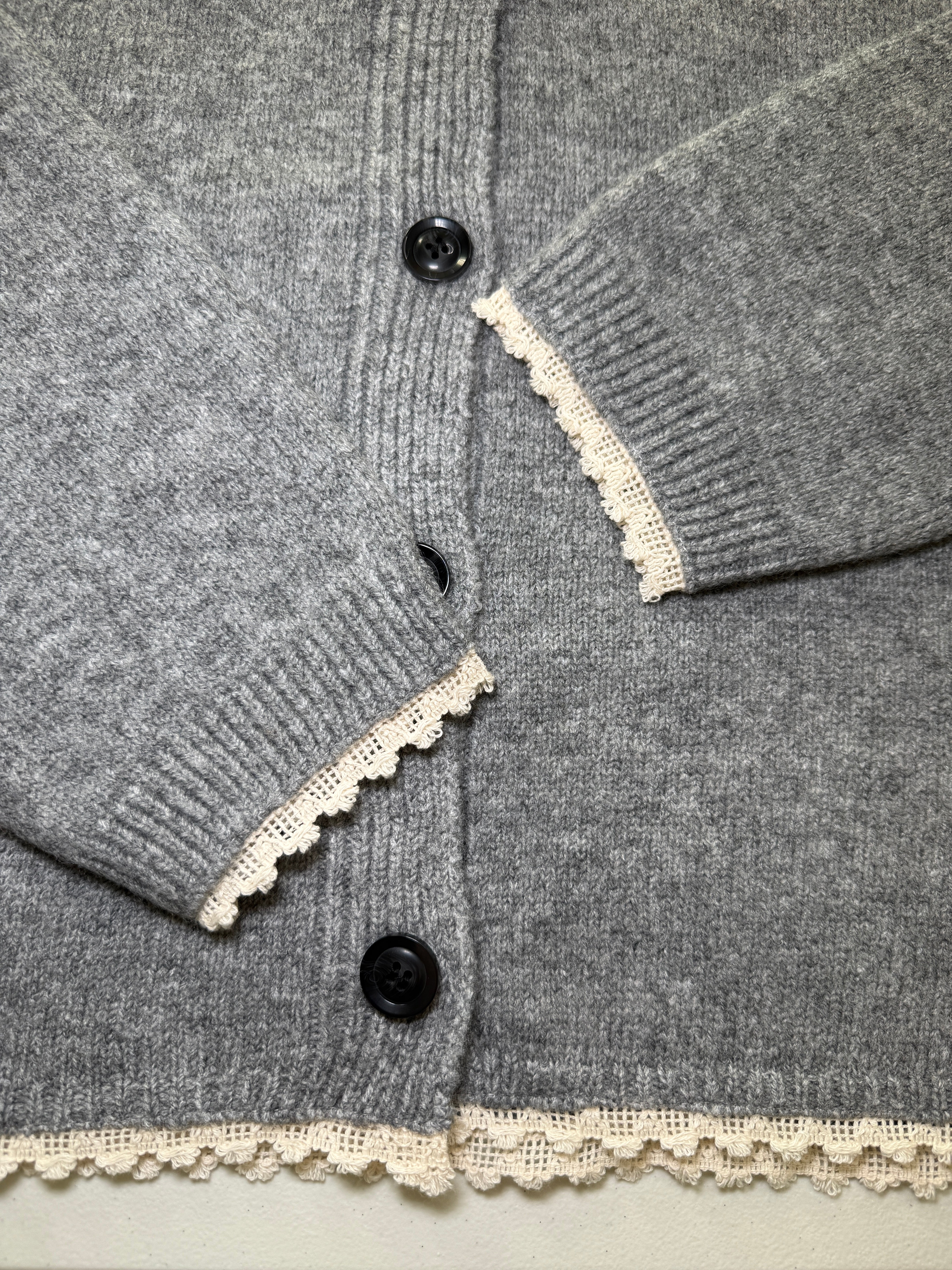 Close-up of the grey knit cardigan showing the lace-edged scarf and black front buttons