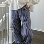 Person wearing a white knit sweater and blue striped pants standing on a staircase.