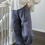 Person wearing a white knit sweater and blue striped pants standing on a staircase.
