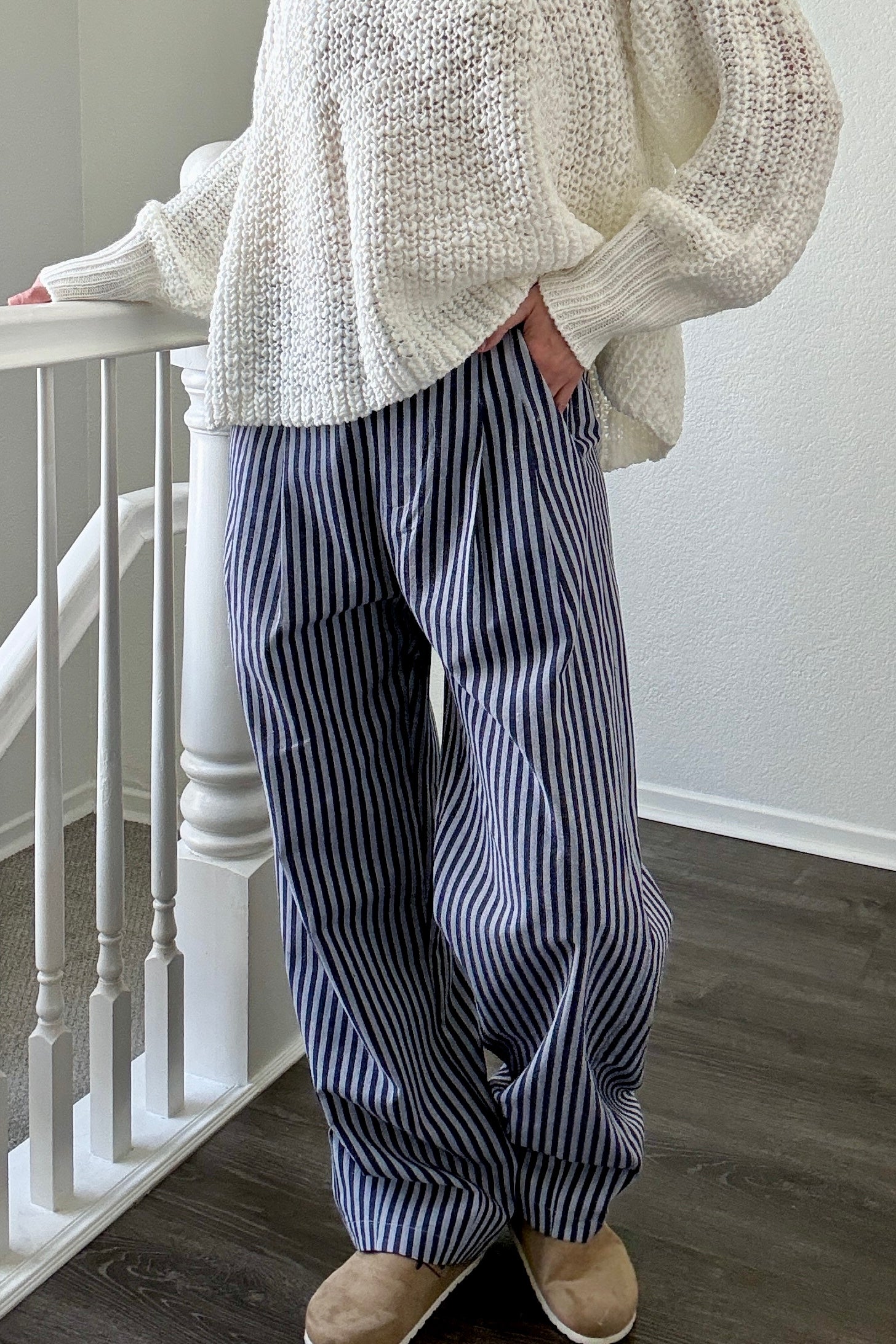 Person wearing a white knit sweater and blue striped pants standing on a staircase.