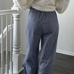 Person wearing a textured sweater and striped pants standing in a room with a staircase.