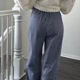 Person wearing a textured sweater and striped pants standing in a room with a staircase.
