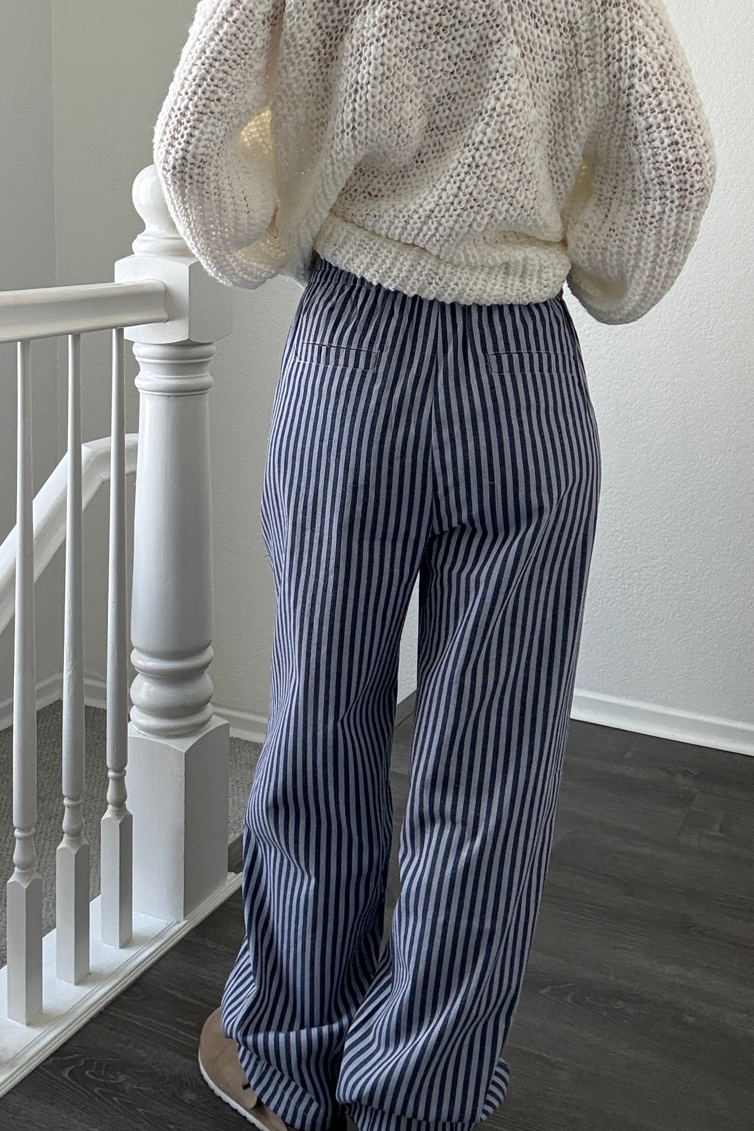 Person wearing a textured sweater and striped pants standing in a room with a staircase.