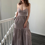 Woman wearing a checkered dress standing in a room with a white railing.
