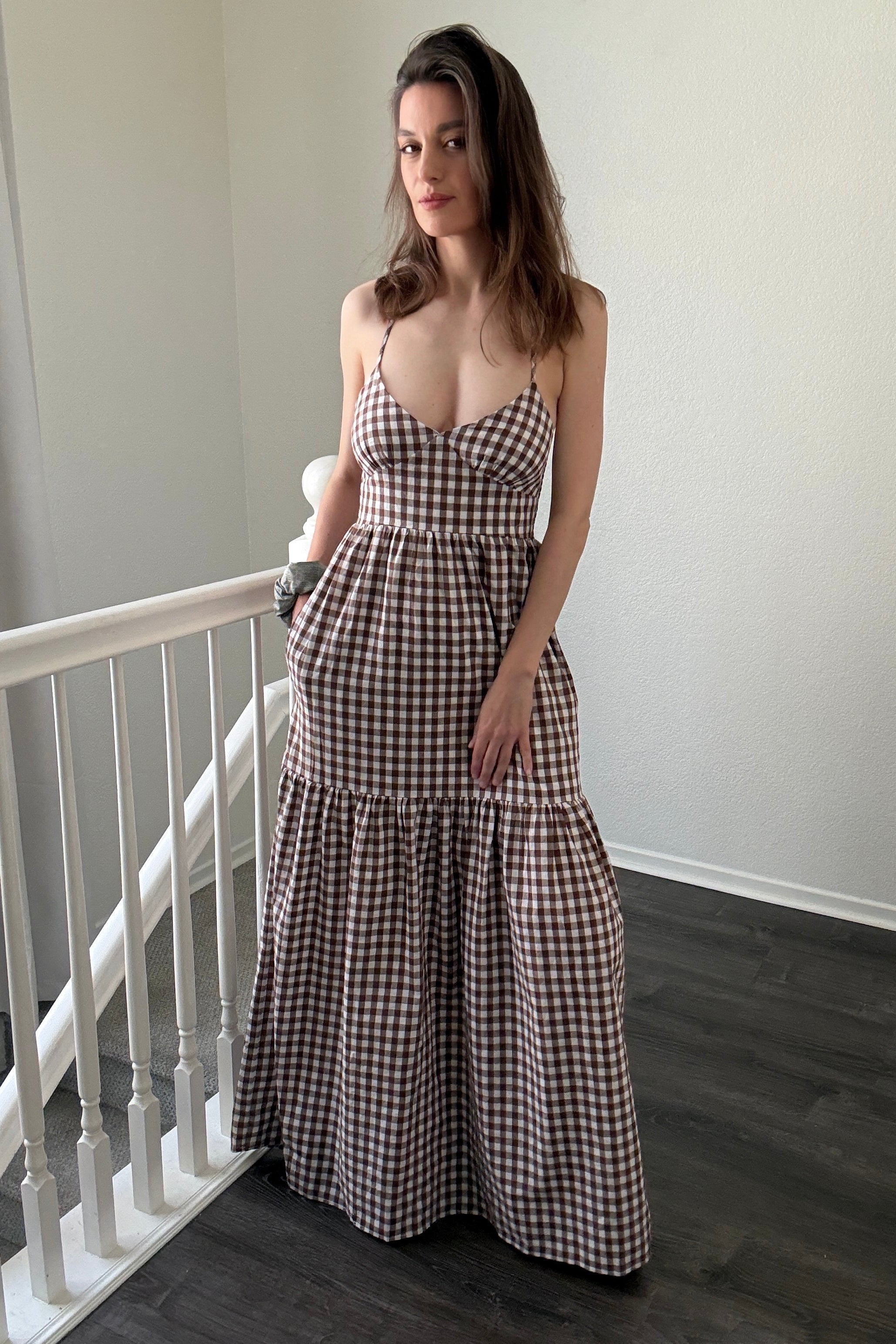 Woman wearing a checkered dress standing in a room with a white railing.