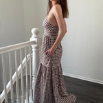 Woman in a checkered dress standing on a staircase with white walls.