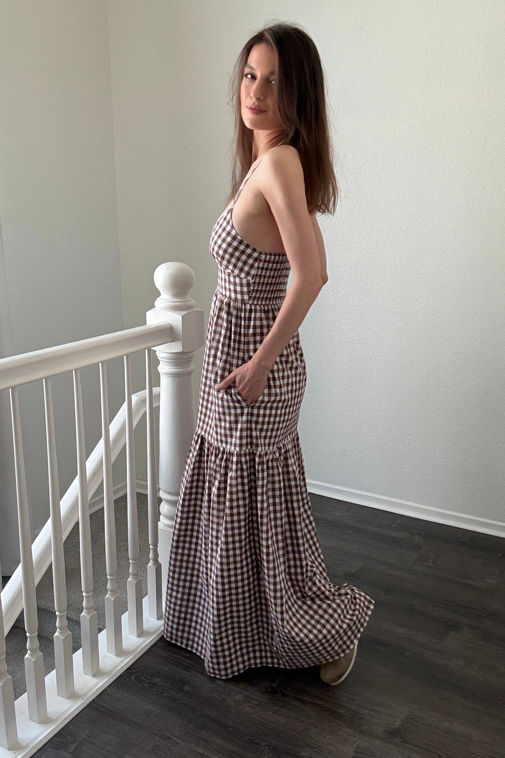 Woman in a checkered dress standing on a staircase with white walls.