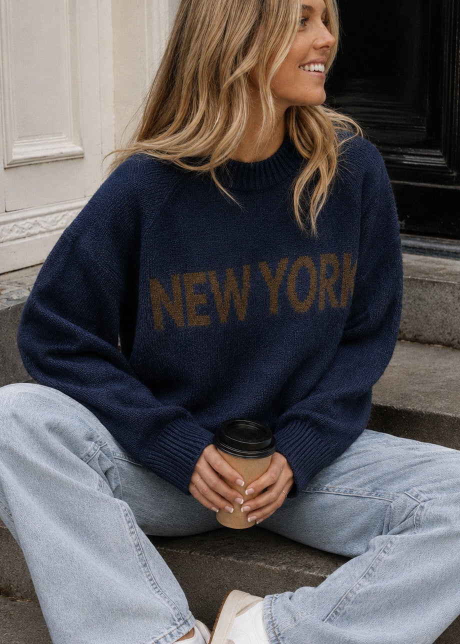 Lifestyle image of woman wearing New York Graphic Sweater in Navy with bold NEW YORK lettering and light-wash jeans
