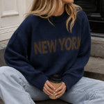 Lifestyle image of woman wearing New York Graphic Sweater in Navy with bold NEW YORK lettering and light-wash jeans