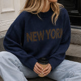 Lifestyle image of woman wearing New York Graphic Sweater in Navy with bold NEW YORK lettering and light-wash jeans