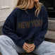 Lifestyle image of woman wearing New York Graphic Sweater in Navy with bold NEW YORK lettering and light-wash jeans