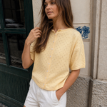 Woman wearing Piper Pointelle Cotton Button Down Cardigan - Light Yellow and white shorts standing against a textured wall.