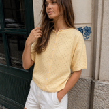 Woman wearing Piper Pointelle Cotton Button Down Cardigan - Light Yellow and white shorts standing against a textured wall.