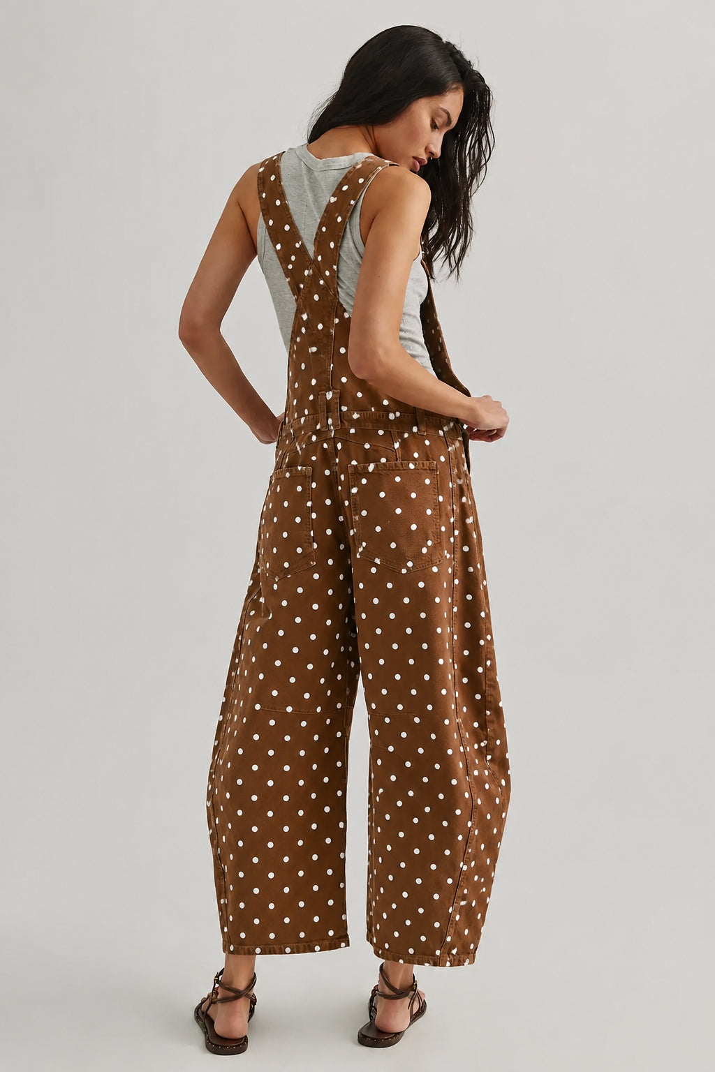 Back view of woman wearing Aaron & Amber brown polka dot barrel-leg denim overalls