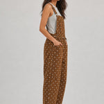 Side view of woman wearing Aaron & Amber brown polka dot barrel-leg denim overalls