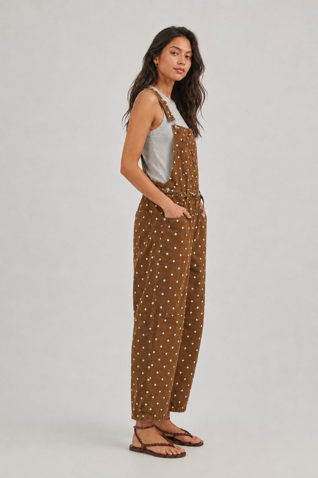 Side view of woman wearing Aaron & Amber brown polka dot barrel-leg denim overalls