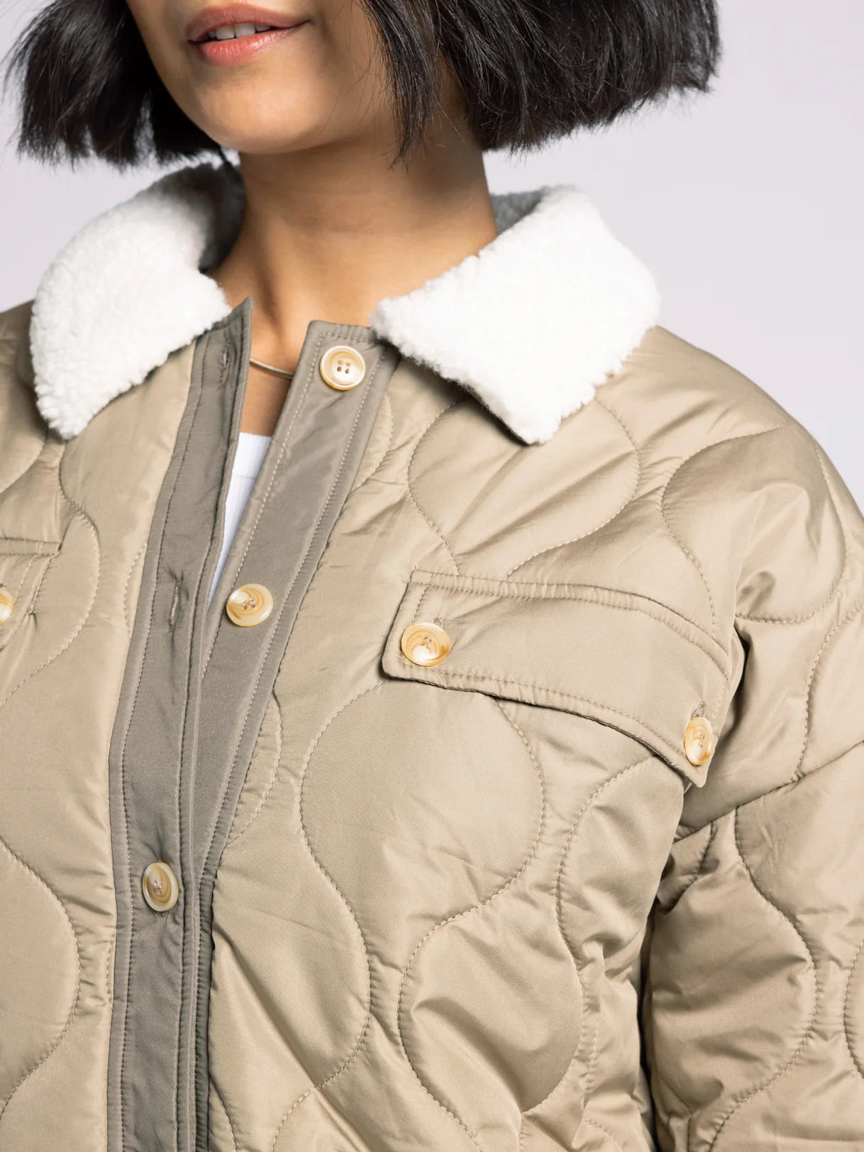 Close-up of sherpa collar and quilted fabric on olive puffer coat — soft, textured women’s outerwear.