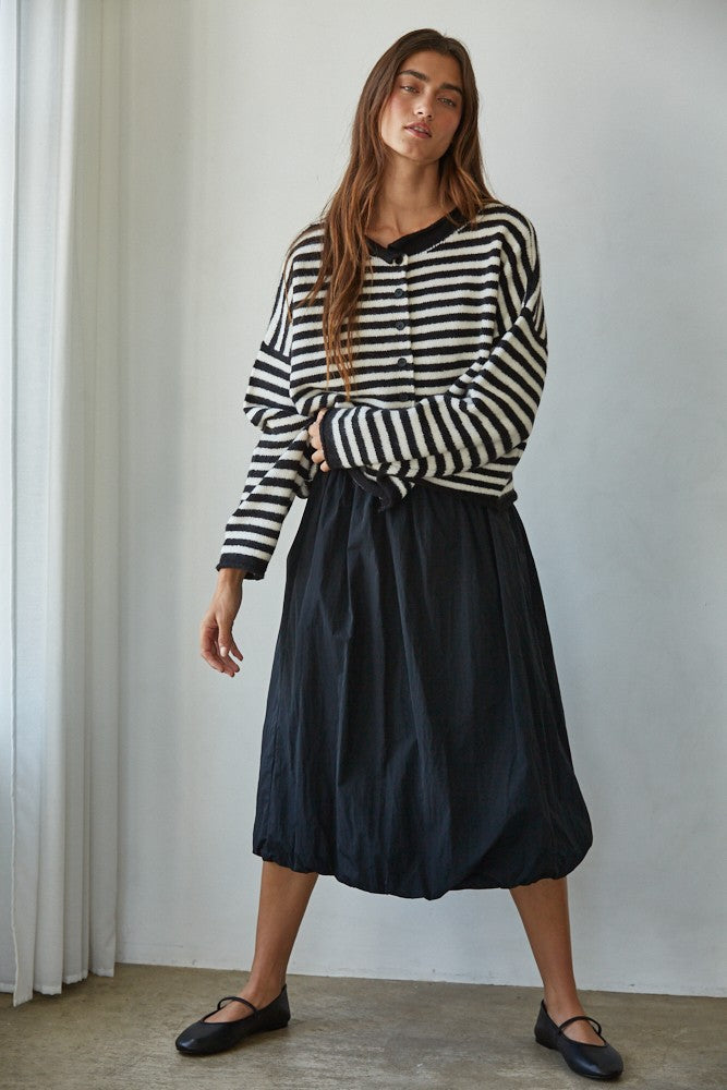 Full-body front view of a woman in a black and white striped knit sweater styled with a black midi skirt