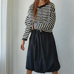 Full-body front view of a woman in a black and white striped knit sweater styled with a black midi skirt