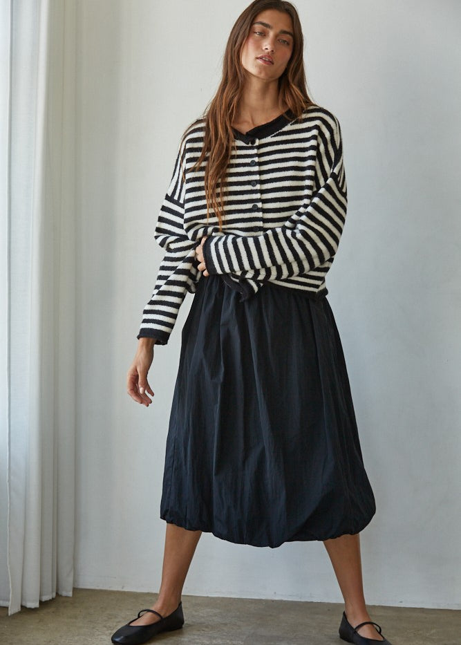 Full-body front view of a woman in a black and white striped knit sweater styled with a black midi skirt