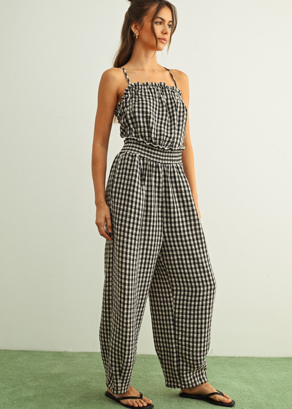 Woman wearing black and white gingham cotton jumpsuit with smocked top and relaxed barrel-leg silhouette