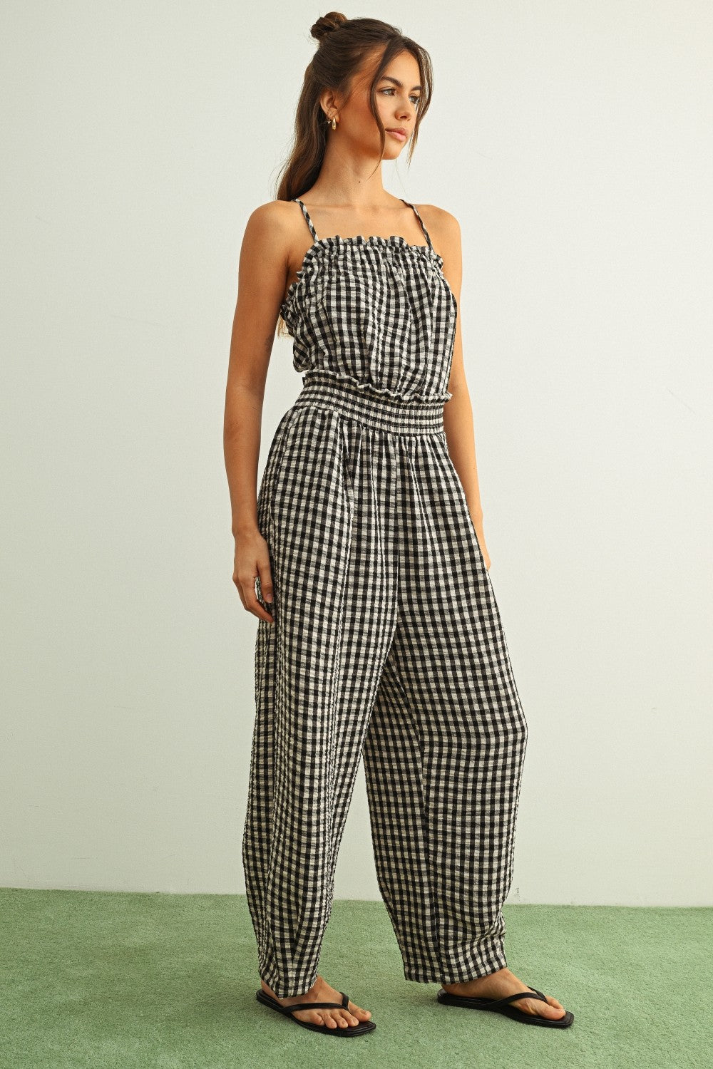 Woman wearing black and white gingham cotton jumpsuit with smocked top and relaxed barrel-leg silhouette