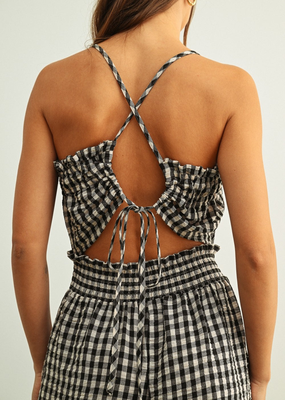 Open back detail of black and white gingham smocked jumpsuit with adjustable criss-cross straps