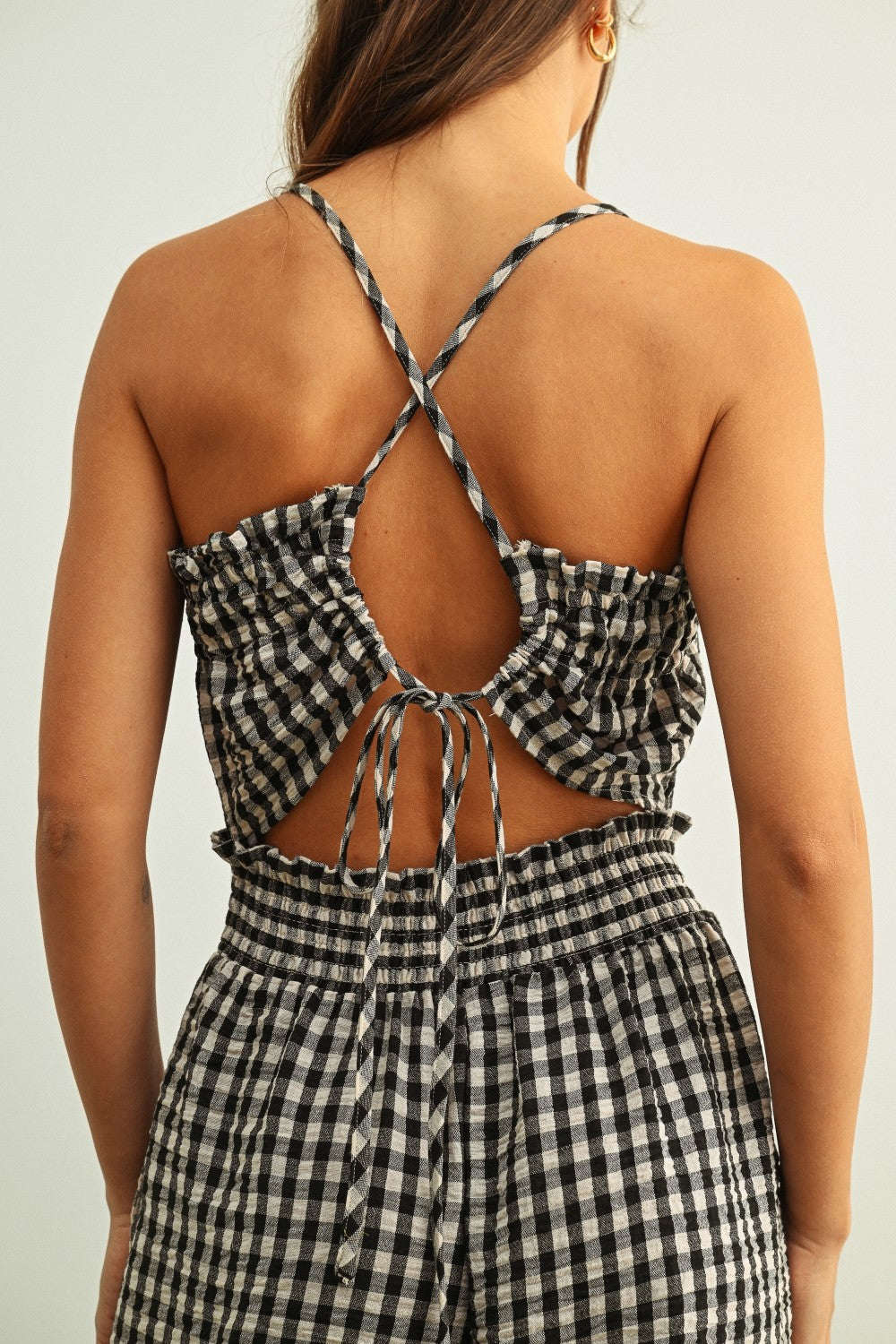 Open back detail of black and white gingham smocked jumpsuit with adjustable criss-cross straps