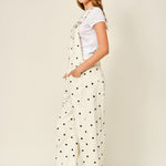 Side view of cream polka dot denim overalls with relaxed barrel legs
