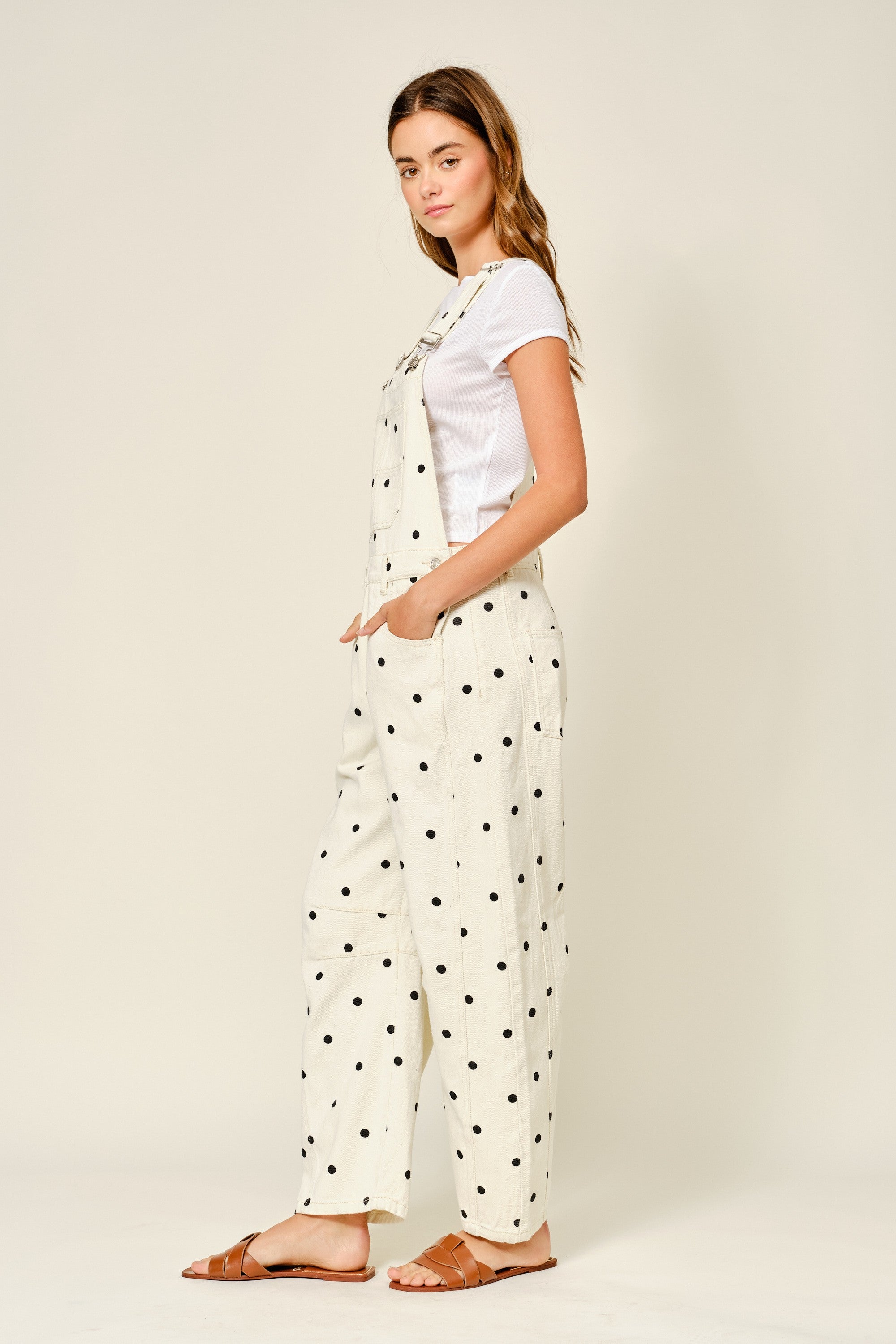 Side view of cream polka dot denim overalls with relaxed barrel legs