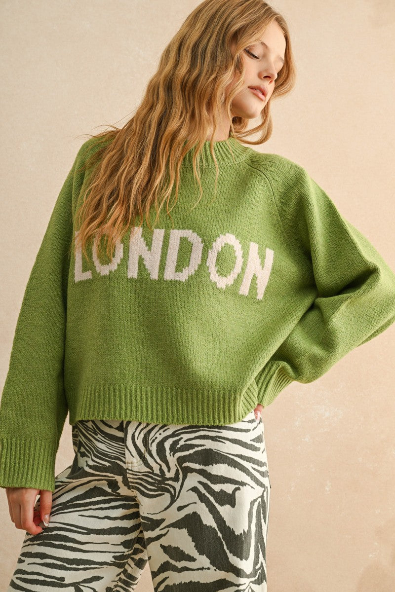 Person wearing a green sweater with 'LONDON' text on a beige background