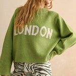Person wearing a green sweater with 'LONDON' text on a beige background