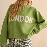 Person wearing a green sweater with 'LONDON' text on a beige background