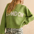 Person wearing a green sweater with 'LONDON' text on a beige background