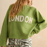 Person wearing a green sweater with 'LONDON' text on a beige background