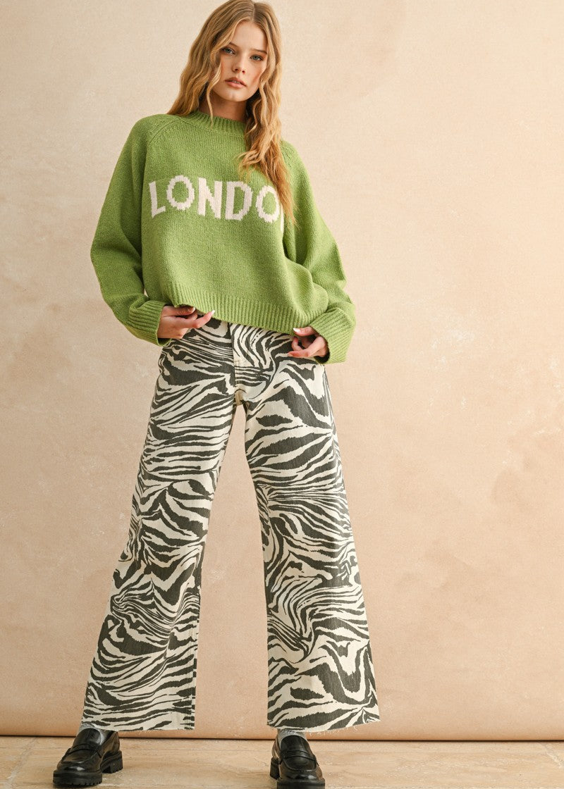 Woman wearing a green sweater with 'LONDON' text and zebra print pants on a beige background