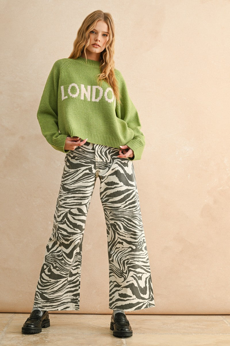 Woman wearing a green sweater with 'LONDON' text and zebra print pants on a beige background